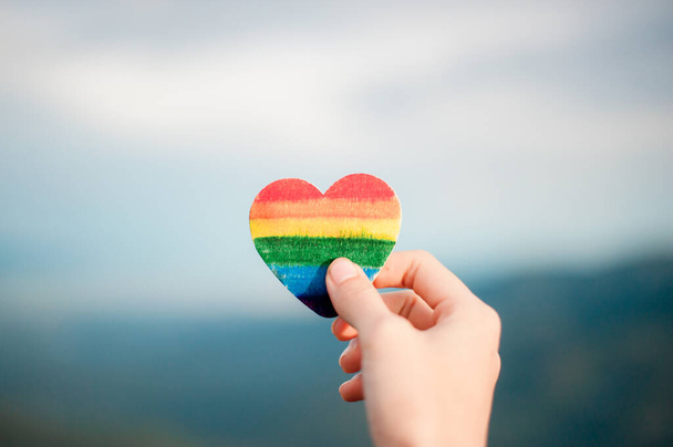 Concepto de derechos LGBT, mano sostiene un corazón pintado de colores del arco iris como una bandera LGBT contra la luz del sol. Copiar espacio - Foto, imagen