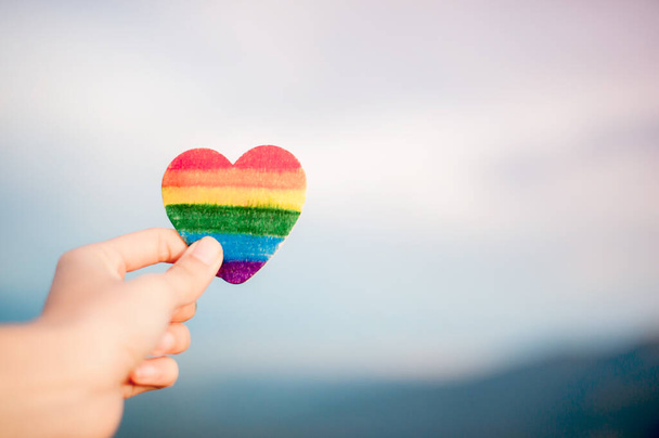 Концепция прав ЛГБТ, рука держит сердце окрашенные радужные цвета, как флаг ЛГБТ против света солнца. Копировальное пространство - Фото, изображение