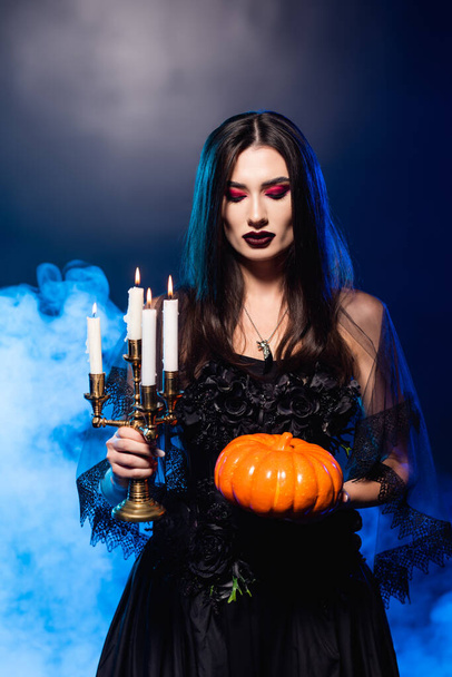sápadt nő fekete smink gazdaság tök és égő gyertyák kék füst, halloween koncepció - Fotó, kép