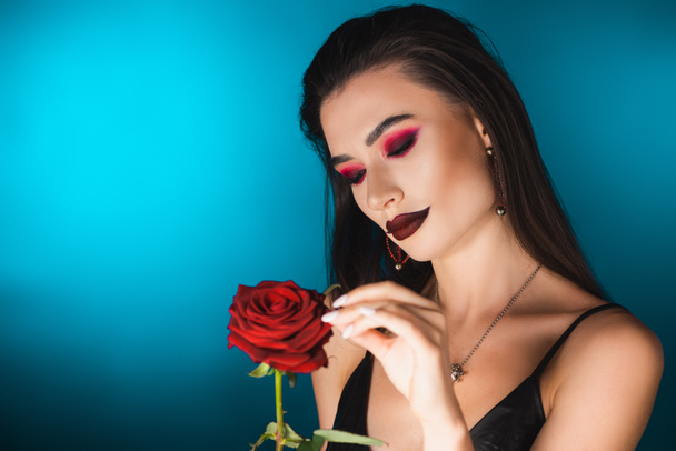 fiatal nő sötét smink megható piros rózsa kék - Fotó, kép