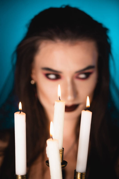 foco seletivo de velas ardentes perto da mulher com maquiagem preta no azul - Foto, Imagem
