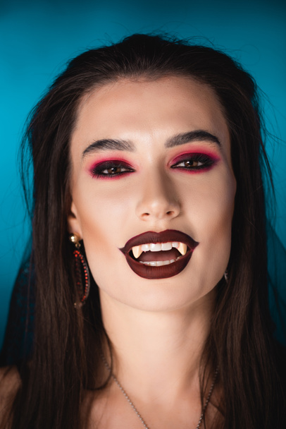 vampiro bruna con trucco nero e denti bianchi spaventosi su blu - Foto, immagini
