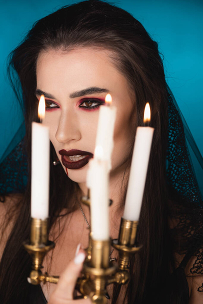 selective focus of woman in veil with blood on face near burning candles on blue - Fotoğraf, Görsel