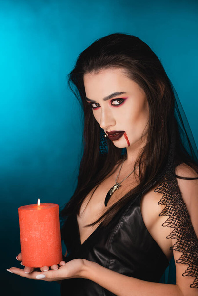 woman with blood on face holding red burning candle on blue - Photo, Image