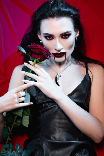 młoda blada kobieta z krwią na twarzy gospodarstwa róża na czerwono - Zdjęcie, obraz