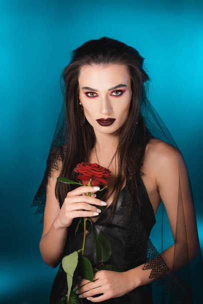 giovane donna bruna con trucco scuro con rosa rossa su blu - Foto, immagini
