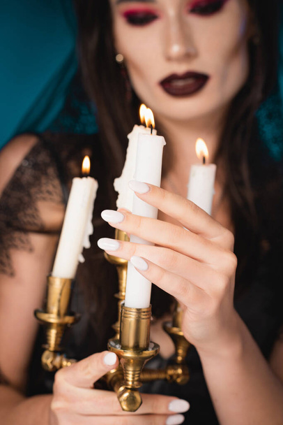 selective focus of pale woman with makeup touching burning candles on blue - Foto, Imagen