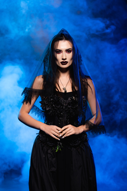 bride in black dress and veil on blue with smoke, halloween concept - Photo, Image