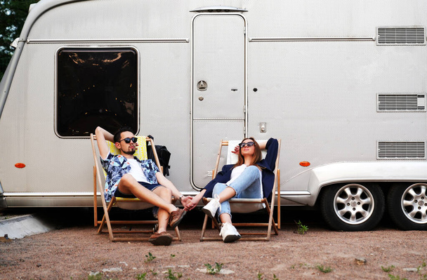  lovers are resting in a recliner chair near their trailer. young family on vacation in the countryside               - Foto, afbeelding