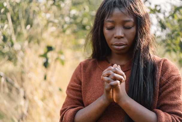 Девушка-афро закрыла глаза и молилась. Руки сложены в молитвенной концепции веры, духовности и религии - Фото, изображение