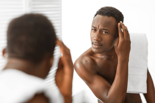 Schwarzer Mann untersucht Haare auf dem Kopf mit Schuppen im Badezimmer - Foto, Bild