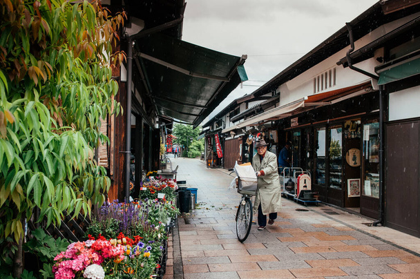 2013年5月29日松本市 – セラミックタイル屋根の古い日本の江戸建築は、縄手通りに植物の花の店になりました。雨の日に自転車で老人 - 写真・画像