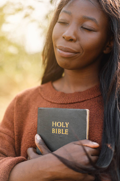 Christliches Afro-Mädchen hält Bibel in ihren Händen. Die Bibel lesen. Konzept für den Glauben. - Foto, Bild
