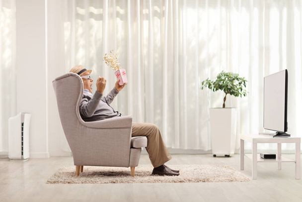 Elderly man at home watching a 3D movie and holding a box of popcorn - Foto, afbeelding