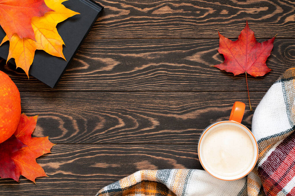 Top view of cup of coffee, book, plaid scarf, pumpkin and colourful leaves on wooden table. Slow living concept. Cozy and warm autumn flat lay with copy space. Fall background. - Foto, imagen