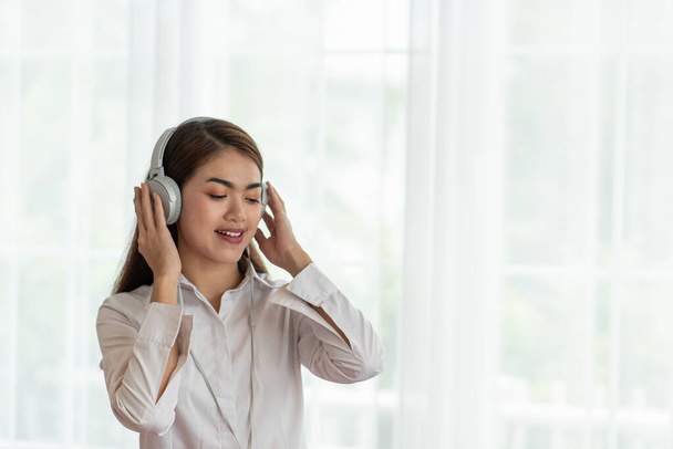 Πορτρέτο της νεαρής Ασιάτισσας να απολαύσετε ακούγοντας μουσική με ακουστικά, χαρούμενες και χαλαρωτικές στιγμές - Φωτογραφία, εικόνα