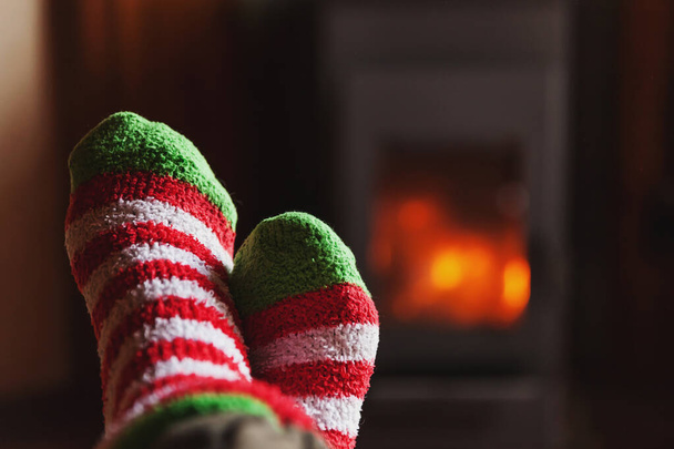 Nohy nohy v zimním oblečení vlněné ponožky na pozadí krbu. Žena sedí doma v zimním nebo podzimním večeru, odpočívá a zahřívá se. Koncept zimního a chladného počasí. Hygge Štědrý večer - Fotografie, Obrázek