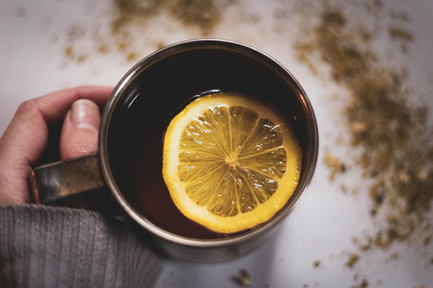 Frau hält Tasse Tee mit Zitronenscheibe in der Hand. Gemütliche und entspannte Atmosphäre. - Foto, Bild