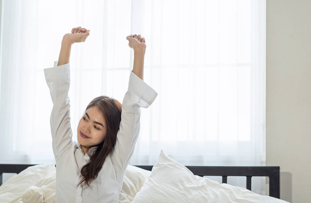 Portrait of young Asian woman stretching in bed after wake up in the morning - Photo, Image