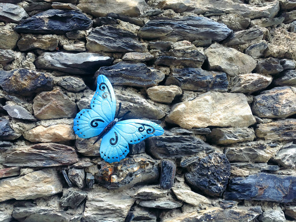 Modrý motýl visící na rustikální kamenné zdi. Doplněk na zdobení domu. Motýl světlé a krásné barvy. - Fotografie, Obrázek