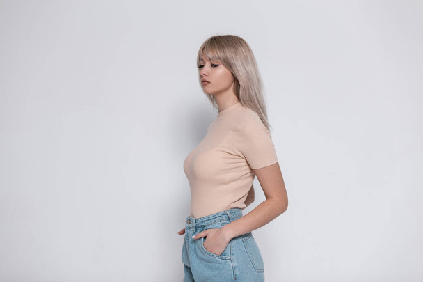 Pretty sexy cute young blond woman in stylish clothes posing near a vintage white wall indoors. Cute girl model with natural make-up with trendy hairstyle in elegant clothes in the room. Youth look. - Foto, Imagen