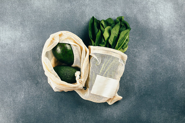 Avocado und Spinat in Öko-Baumwolltaschen auf dem Tisch. Zero Waste-Shopping-Konzept. Flache Lage, Draufsicht. - Foto, Bild