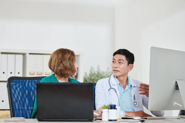 Azjatyccy pracownicy medyczni siedzący w biurze i dyskutujący o leczeniu pacjenta - Zdjęcie, obraz