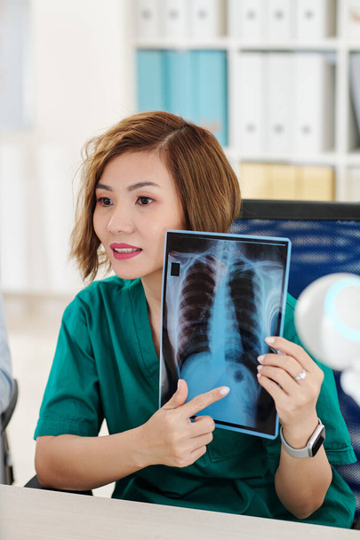 Radyolog video görüşmesi yapıyor ve hastanın göğüs röntgenindeki koyu noktayı işaret ediyor. - Fotoğraf, Görsel