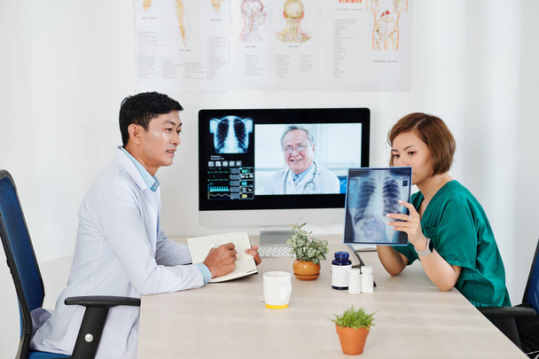 Equipo médico de video llamando a oncólogo experimentado para discutir la mancha oscura en la radiografía de tórax del paciente - Foto, Imagen