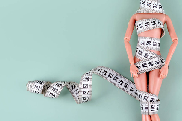 Doll wrapped in measuring tape. Tied up plastic doll, weight loss, fasting and slimming, diet, anorexia, eating disorder, overeating control, female fight for perfect fit body concept. Free copyspace. - Photo, Image