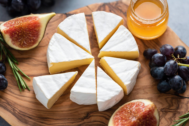 Camembert or brie cheese with figs, grapes and honey on wooden serving board. Cheese plate - Photo, Image