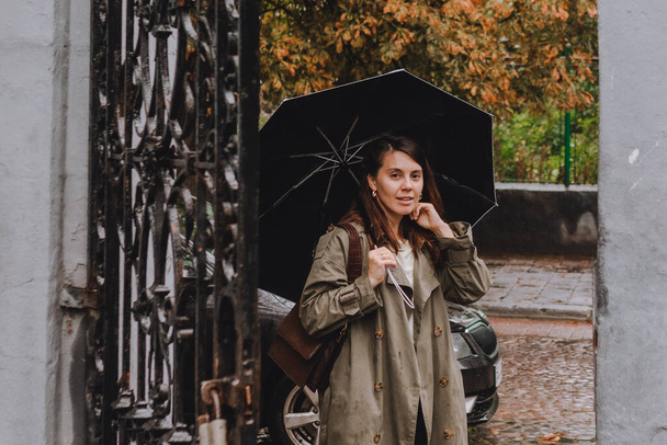 junge hübsche Frau im herbstlichen Outfit, die bei regnerischem Wetter mit Regenschirm durch die Straßen der Stadt läuft. Kopierraum - Foto, Bild