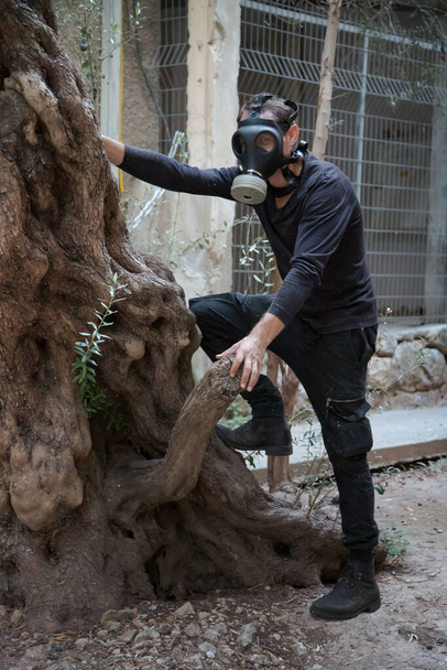 Umweltkatastrophe. Postapokalyptischer Überlebender in Gasmaske. Mann in Sauerstoffmaske klettert auf einen Baum. Gefährlicher Job - Foto, Bild