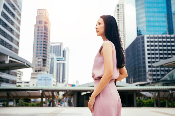 Businesswoman looking across towards city with tall modern buildings, head and shoulders of young adult woman. - Foto, imagen