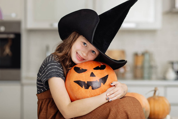 Fijne Halloween. Schattig klein meisje in heksenkostuum met gesneden pompoen. gelukkig familie voorbereiding voor Halloween - Foto, afbeelding