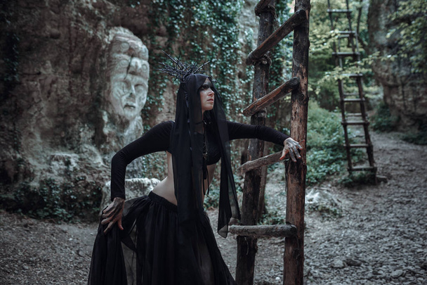 Záhadná čarodějka čarodějka čarodějnice krásné černé šaty procházka v tmavém lese. Dáma v gotickém vzhledu. Oblečení pro halloween. - Fotografie, Obrázek