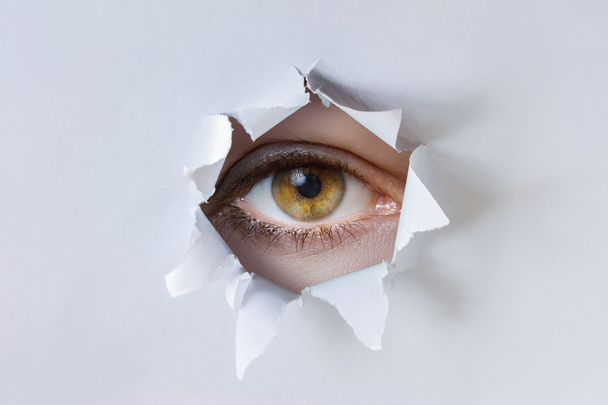 A woman eye observes through a hole in the paper. - Фото, зображення