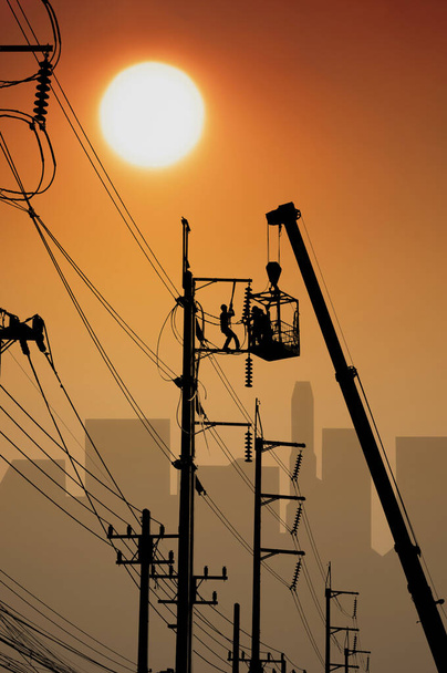 Eletricistas silhuetas no caminhão guindaste estão trabalhando para o sistema elétrico de manutenção no poste de energia com sombra de edifício borrada no fundo do céu do nascer do sol, modo de ilustração - Foto, Imagem