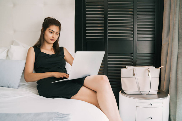 Portrait of young businesswoman working on her laptop at the hotel room. Business travel concept. - Fotó, kép