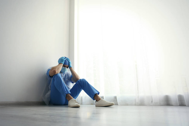 Yorgun doktor içeride yerde oturuyor, mesaj için yer var. COVID-19 salgını sırasında sağlık çalışanlarının stresi - Fotoğraf, Görsel