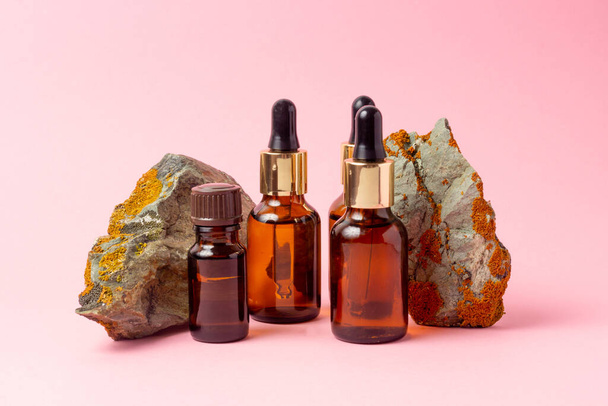 An amber bottle for essential oils and cosmetics stands next to the stone. Glass bottle on a pink background. Dropper, spray bottle. Natural cosmetics concept. - Valokuva, kuva