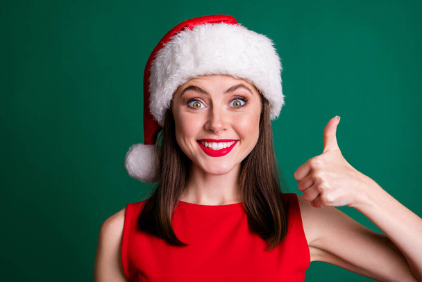 Close-up portrait of her she nice attractive charming lovely content funky ecstatic cheerful cheery girl wearing Santa cap showing thumbup cool isolated over green color background - Fotografie, Obrázek