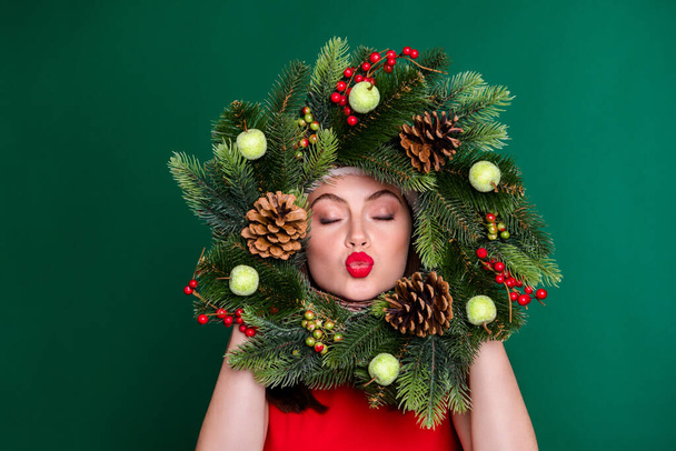 Close-up portrait of her she nice attractive pretty lovable flirty coquettish dreamy girl holding in hands festive wreath having fun sending air kiss isolated over green color background - Valokuva, kuva