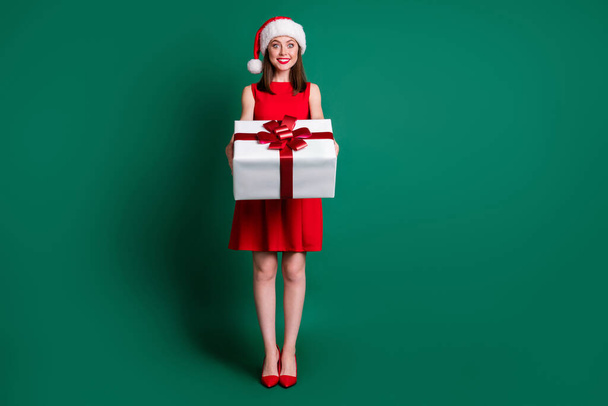 Full size photo cute girl in santa claus headwear hold big gift box want give wish magic present friend x-mas christmas newyear event wear skirt high-heels isolated dark green color background - Foto, Imagen