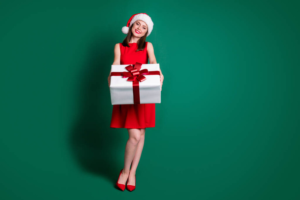 Full length photo positive girl in santa claus headwear celebrate x-mas christmas newyear party give big gift box friend wear stilettos high-heels skirt isolated green color background - Foto, afbeelding