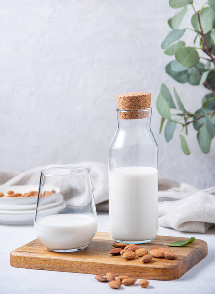 a glass and bottle of fresh vegan almond milk and a few scattered nuts on a white wooden background. Front view and copy space - Foto, Bild