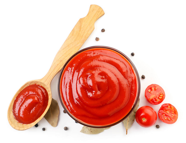 Ketchup in a plate and spoon with tomatoes and laurel leaves on a white background, isolated. Top view - Photo, Image