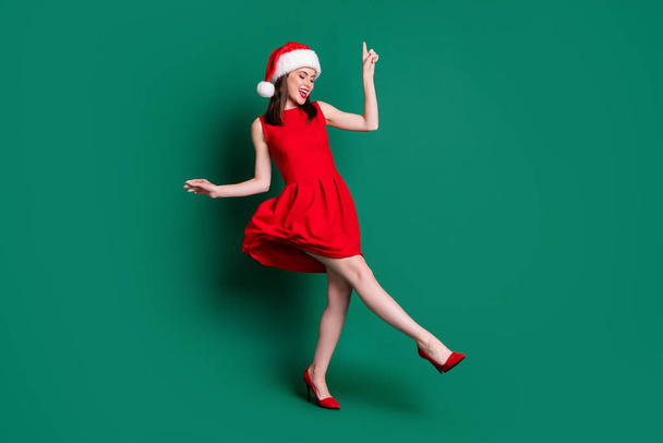 Full body photo of cute attractive lady newyear party festive good mood dancing discotheque youth popular song wear santa cap red mini dress costume stilettos isolated green color background - Foto, immagini