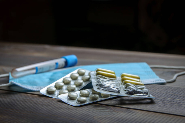 Pillen in einer Blase und eine medizinische Maske auf einem Holztisch. Prävention von Krankheiten. Virus. - Foto, Bild