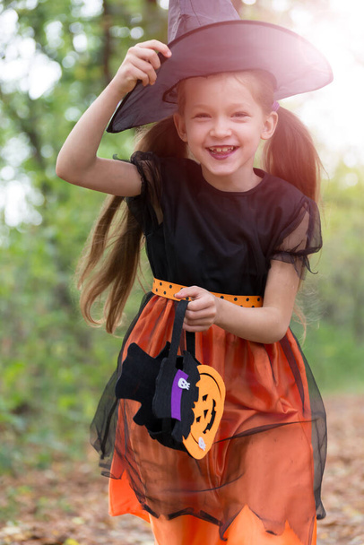 Szczęśliwa dziewczynka w stroju czarownicy i koszu na słodycze na świeżym powietrzu. - Zdjęcie, obraz